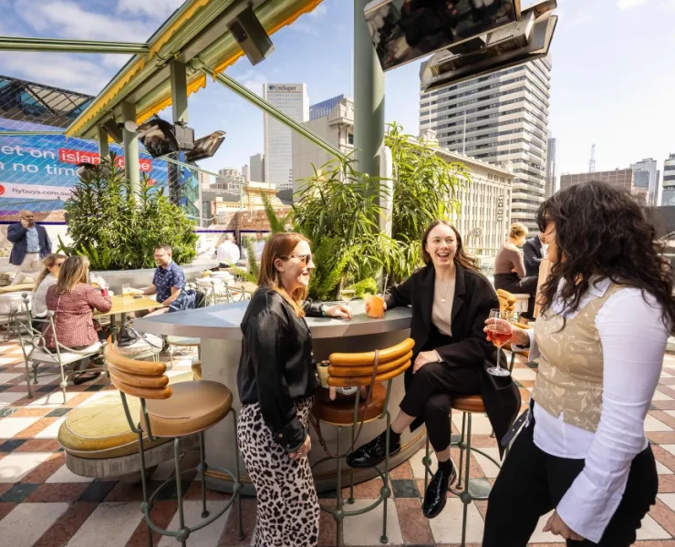 Three female office workers enjoying drinks at a booth at rooftop bar